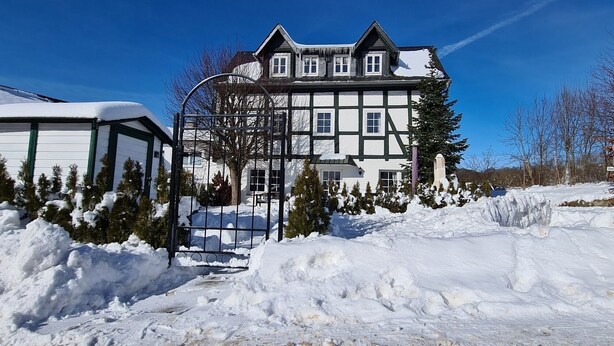 Ein großes, zweistöckiges Gebäude mit einer symmetrischen Fassade, einem mit Schnee bedeckten Dach und einem befestigten Eingang.