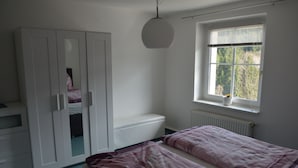 Et soveværelse med seng, skab, vindue med rullegardiner og en radiator.
