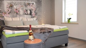 A bedroom with a grey sofa bed, a small round table with a bottle, a window with a potted plant, and a wall mural. - "Pure nature" ... Vacation in the Harz Mountains (Stiege)