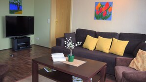 A living room with a dark-colored sofa, a flat-screen TV, a coffee table, and a potted plant. - "Pure nature" ... Vacation in the Harz Mountains (Stiege)