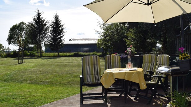 An outdoor patio with a table and chairs, a large umbrella, and a view of a building in the background. - "Pure nature" ... Vacation in the Harz Mountains (Stiege)
