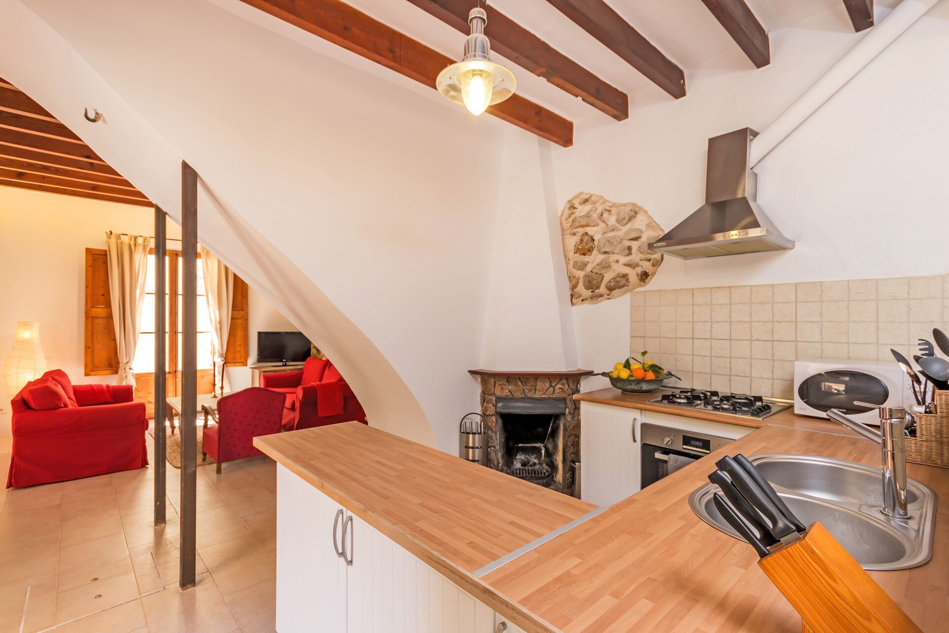 Une cuisine avec un plan de travail en bois, une cuisinière et un évier. Un canapé rouge se trouve dans le salon attenant.