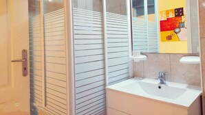 Een moderne badkamer met een douchecabine van glas, een wit wastafelmeubel en een spiegel met een kleurrijk abstract ontwerp op de muur.