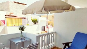 Een balkon met een blauwe lounge stoel, een klein tafeltje met stoelen en een beige parasol.