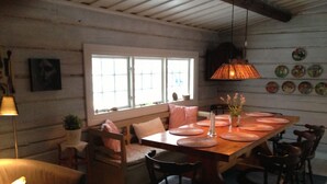 A dining area with a wooden table set for six, surrounded by chairs. There is a bench with cushions, a hanging lamp, and a window with blinds.