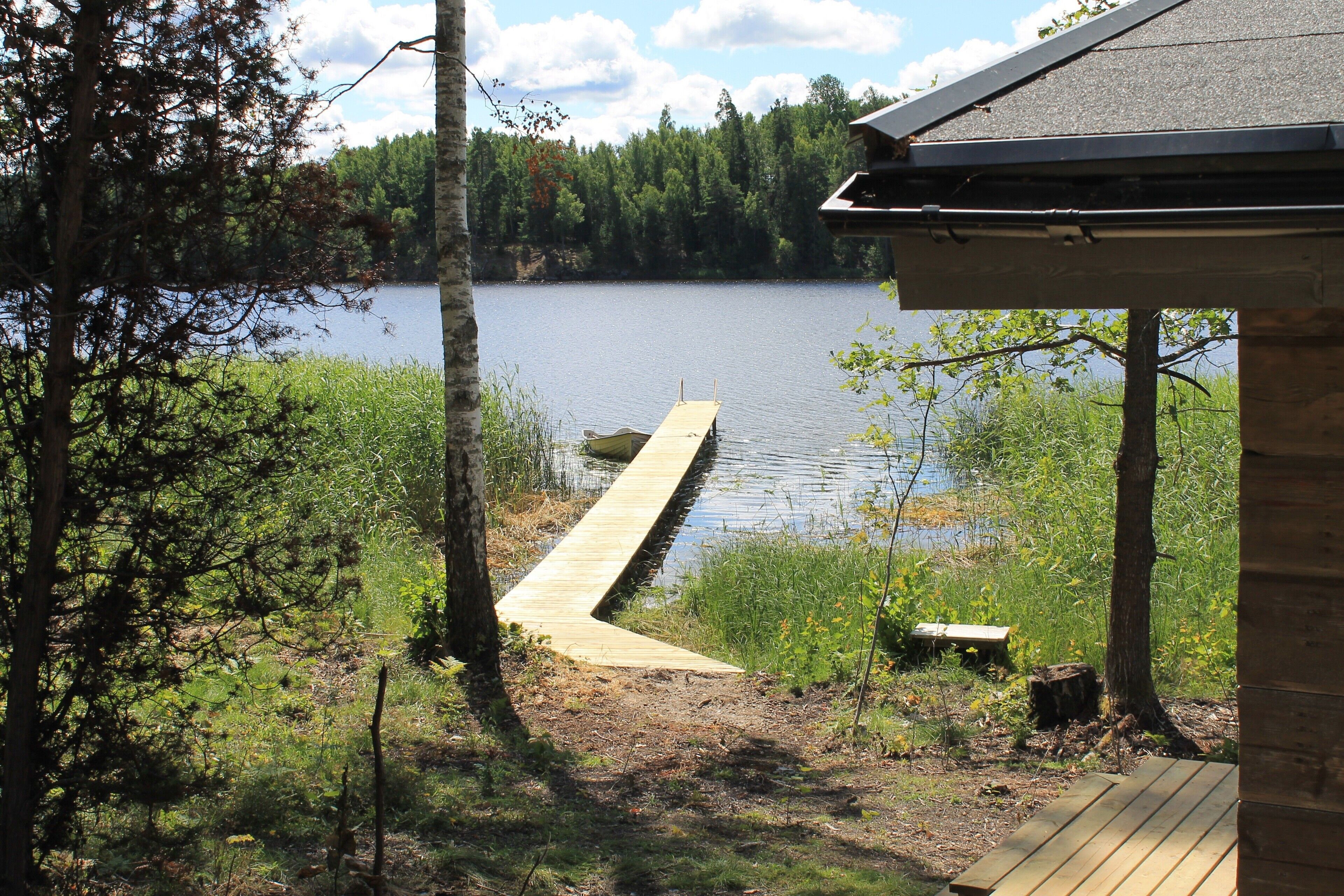 A wooden dock extending into a calm lake, surrounded by trees and a wooden building.