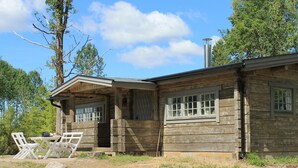 A rustic log cabin with a porch, a table with chairs, and a chimney.