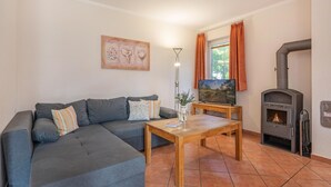 Ein Wohnzimmer mit einem grauen Ecksofa, einem Holztisch, einem Flachbildfernseher, einem Kamin und einem Fenster mit Vorhängen.