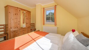 Ein Schlafzimmer mit einem Bett, einem Holzschrank, einem Fenster mit Vorhängen und einer Heizung.