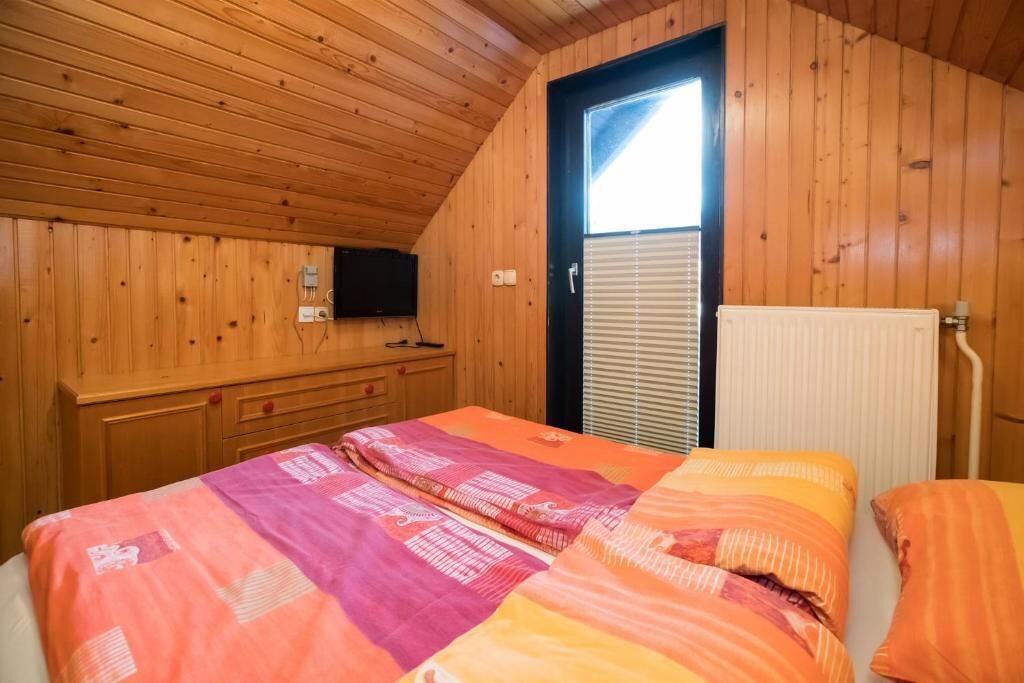 Una habitación con paneles de madera, una cama, un televisor en la pared y una ventana con persianas.