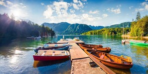 A wooden dock with several boats moored at the end, surrounded by a calm lake and forested hills in the background.