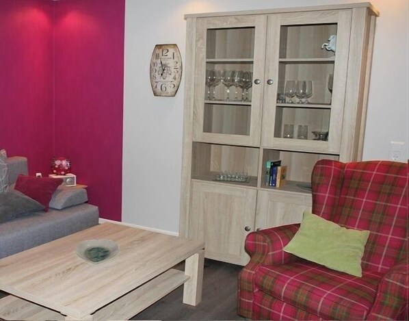 Ein Wohnzimmer mit einem Karo-Sofa, einem Holztisch, einem Schrank mit Glastüren und einer Wanduhr.