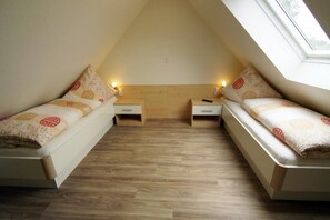 Une petite chambre accueillante, dotée de deux lits simples, d’un plancher en bois et d’un plafond en pente avec une lucarne.