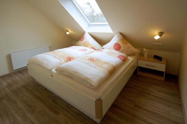A bedroom with a skylight, a bed with patterned bedding, a bedside table with a lamp, and a nightstand.