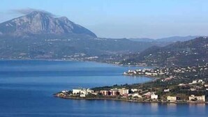 Un pueblo costero con una montaña destacada al fondo, mar tranquilo y una combinación de edificios residenciales y comerciales.