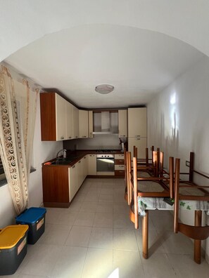 Een kleine keuken met een eethoek, met kastjes, een fornuis en een tafel met stoelen.