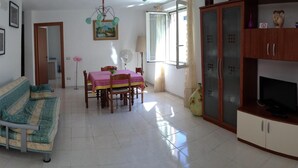 A spacious living area with a dining table, sofa, and TV stand. - 'Absolutely great holiday home with a large garden near the beach' (Policastro Bussentino)