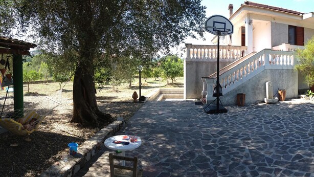 Un patio con un aro de baloncesto, piso de piedra y una escalera que lleva a un edificio.