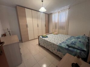 Ein Schlafzimmer mit einem Bett, einem Kleiderschrank, einem Schreibtisch und einer Pendelleuchte.