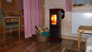 Una habitación acogedora con una estufa de leña, cortinas a cuadros, una cesta de mimbre y una silla de madera.