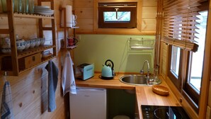 Una cocina compacta con paredes de madera, un lavamanos empotrado, un tostador y una ventana con persianas.