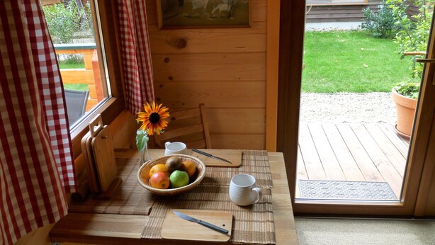 Una mesa de madera con un bol de fruta, un cuchillo, una taza y un girasol.