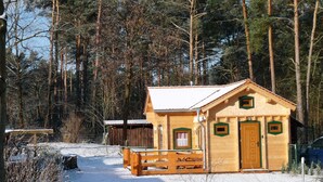Una cabaña de madera con porche, rodeada por un bosque nevado.