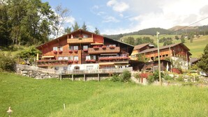 Un bâtiment en bois à plusieurs étages, doté de balcons, entouré d’un champ verdoyant et d’arbres.