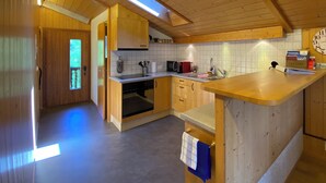 Une cuisine de taille réduite, dotée de meubles en bois, d’un four à micro-ondes, d’un évier et d’une fenêtre située au-dessus du plan de travail.