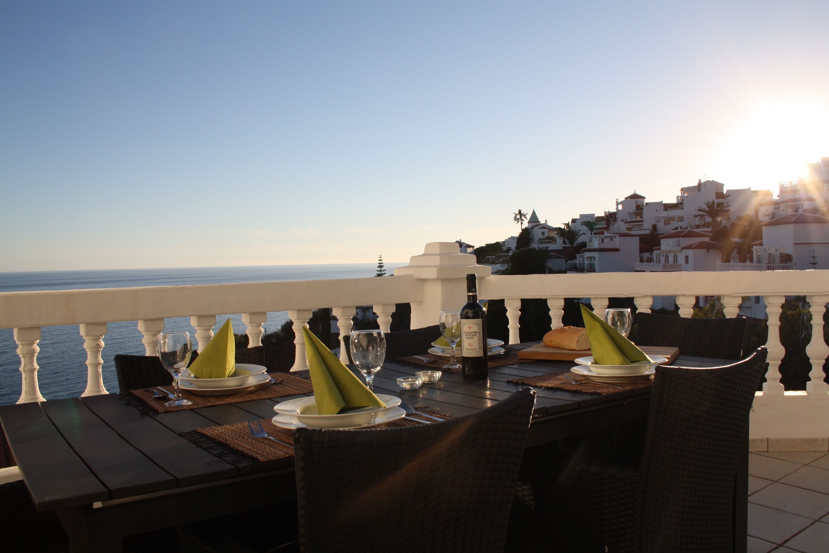 A dining table set with plates, glasses, and a bottle, overlooking a coastal view with buildings in the background.