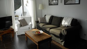 Ein Wohnzimmer mit einer Couch, einem Couchtisch mit Früchten, einem Fernseher und zwei gerahmten Bildern an der Wand.