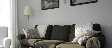 A living room with a sofa, a coffee table with a fruit bowl, a lamp, and two framed pictures on the wall.