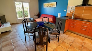 Un coin repas avec une table ronde et des chaises, une cuisine avec des meubles orange et un tableau accroché au mur bleu.