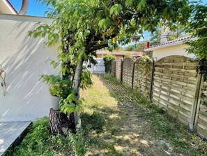 A backyard with a tree, a brick wall, and a wooden gate. - Gorgeous house a few steps only to the beach G0126 (Hourtin)