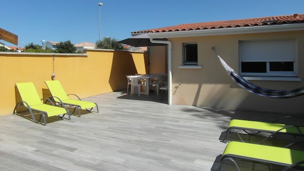 Une terrasse avec deux chaises longues jaunes, une petite table et un hamac.