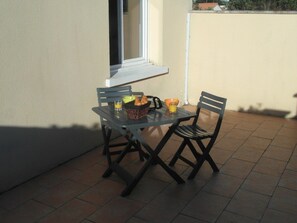 A small outdoor patio with a table and two chairs, a basket with bread, and a glass of orange juice. - Gorgeous house a few steps only to the beach G0126 (Hourtin)