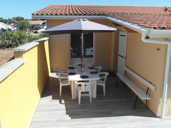 Une terrasse avec une table et des chaises, un banc et un espace couvert équipé d’une table et de chaises.
