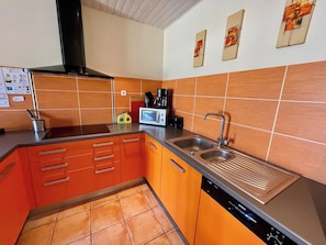 Una cocina con armarios color naranja, un lavavajillas Bosch, un lavamanos y una cafetera.