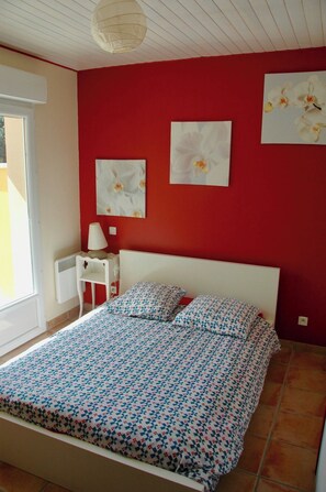 Ein Schlafzimmer mit einem Bett, einem Nachttisch, einer Lampe und zwei Wandbildern von Blumen.