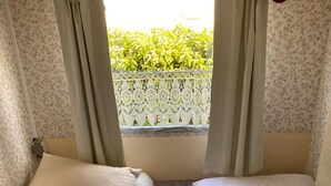 Una habitación pequeña con dos camas, papel tapiz floral y una ventana con cortinas.