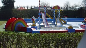 Un parque infantil al aire libre con toboganes, una estructura de juego con forma de arcoíris y una bandera en un mástil.