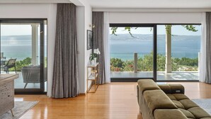 Ein modernes Wohnzimmer mit einer großen Couch, einem Essbereich mit Tisch und Stühlen sowie Meerblick durch große Fenster.