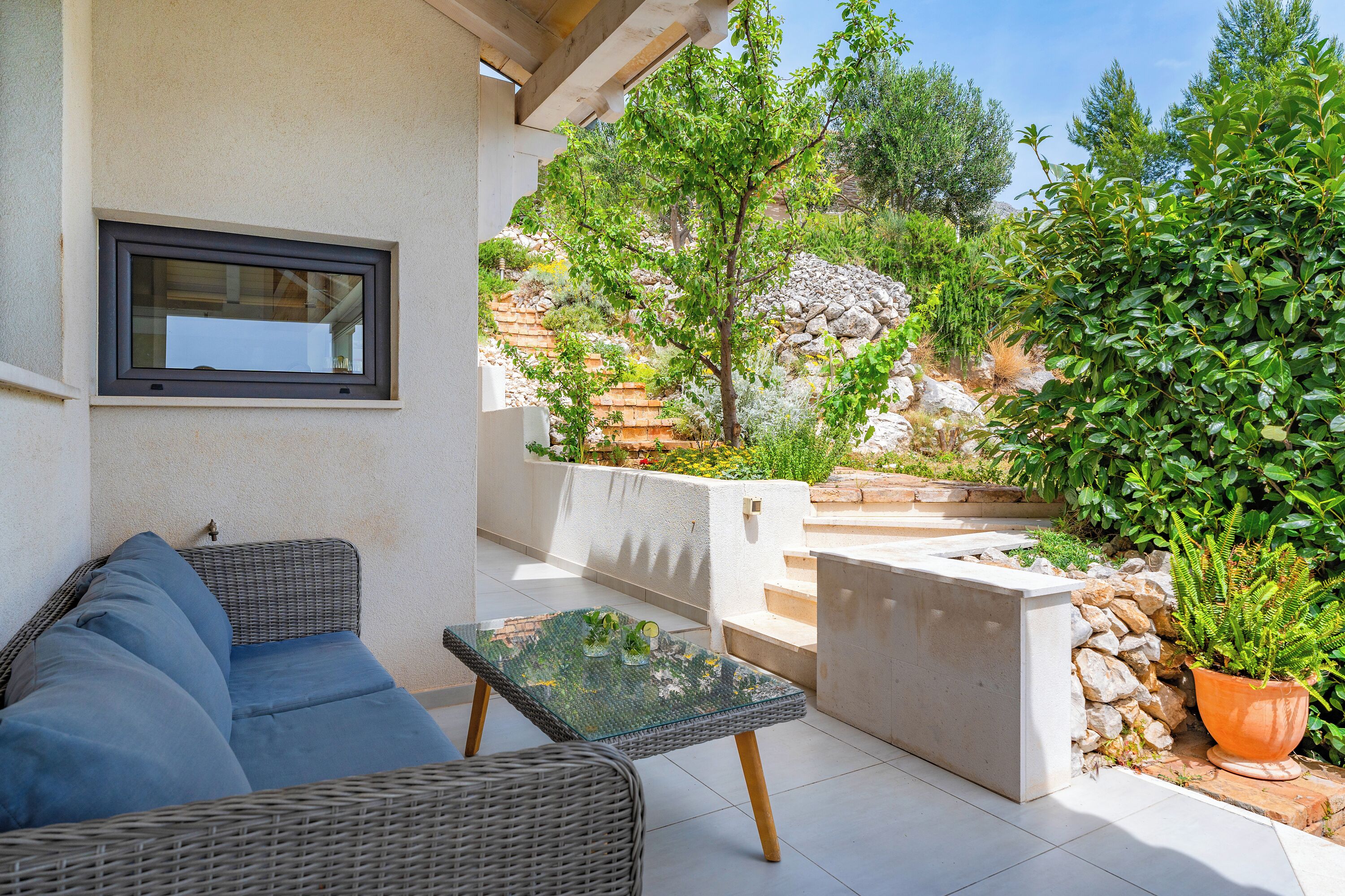 A patio area with a wicker sofa, a glass-top table, and a potted plant.