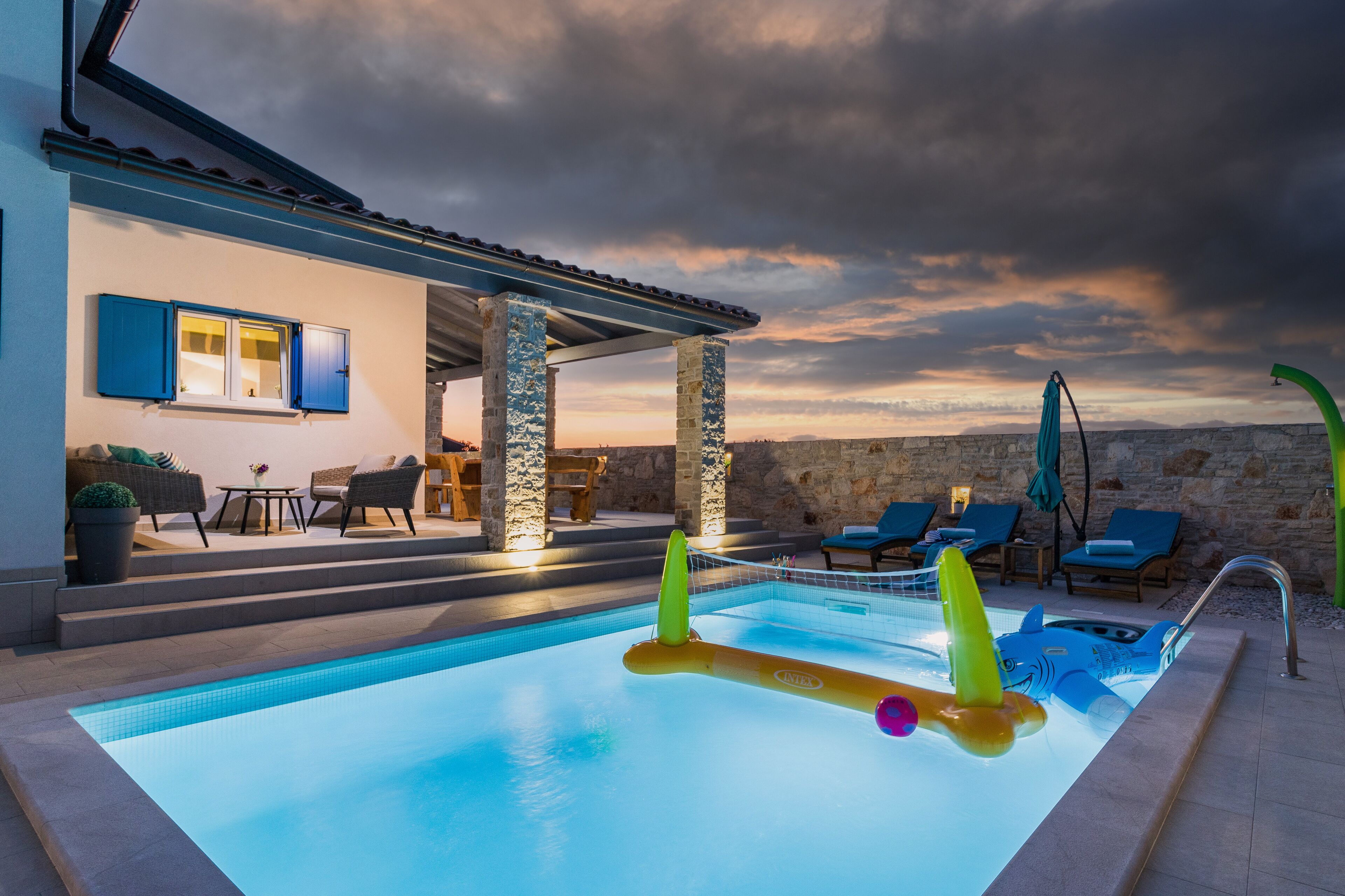 Piscina com cadeiras de descanso e um muro de pedra ao fundo.