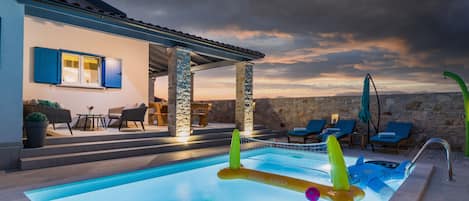 A swimming pool with lounge chairs and a stone wall in the background.