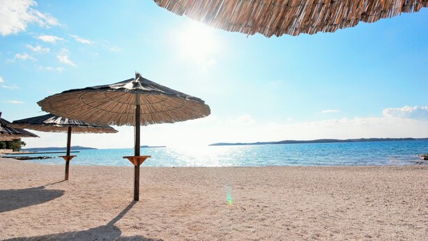 Una spiaggia con ombrelloni di paglia e una vista limpida sul mare.