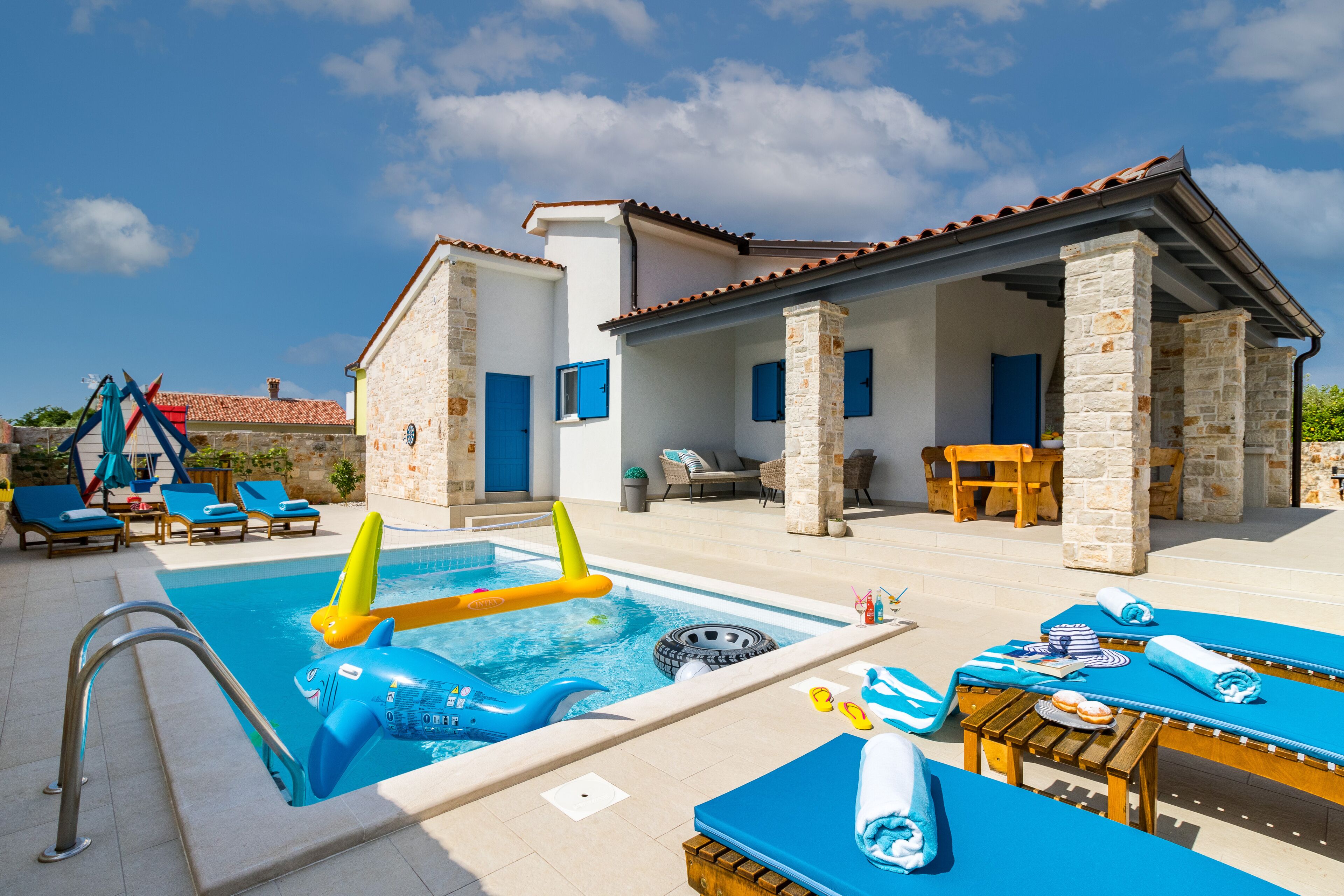 A pool area with lounge chairs, a hot tub, and a stone building with a tiled roof.