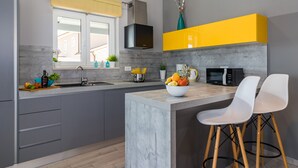 Una cucina moderna con mobili grigi, una parete gialla a contrasto, un forno a microonde integrato e una ciotola di frutta sull'isola.