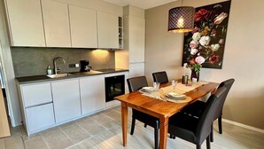 A modern kitchen with white cabinets, a dining table with chairs, and a pendant light. - Apartment only 600 m. from the beach, with sunny balcony on the south! (Nordholland)