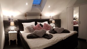 A bedroom with a skylight, a bed with multiple pillows, bedside tables with lamps, and a wardrobe.